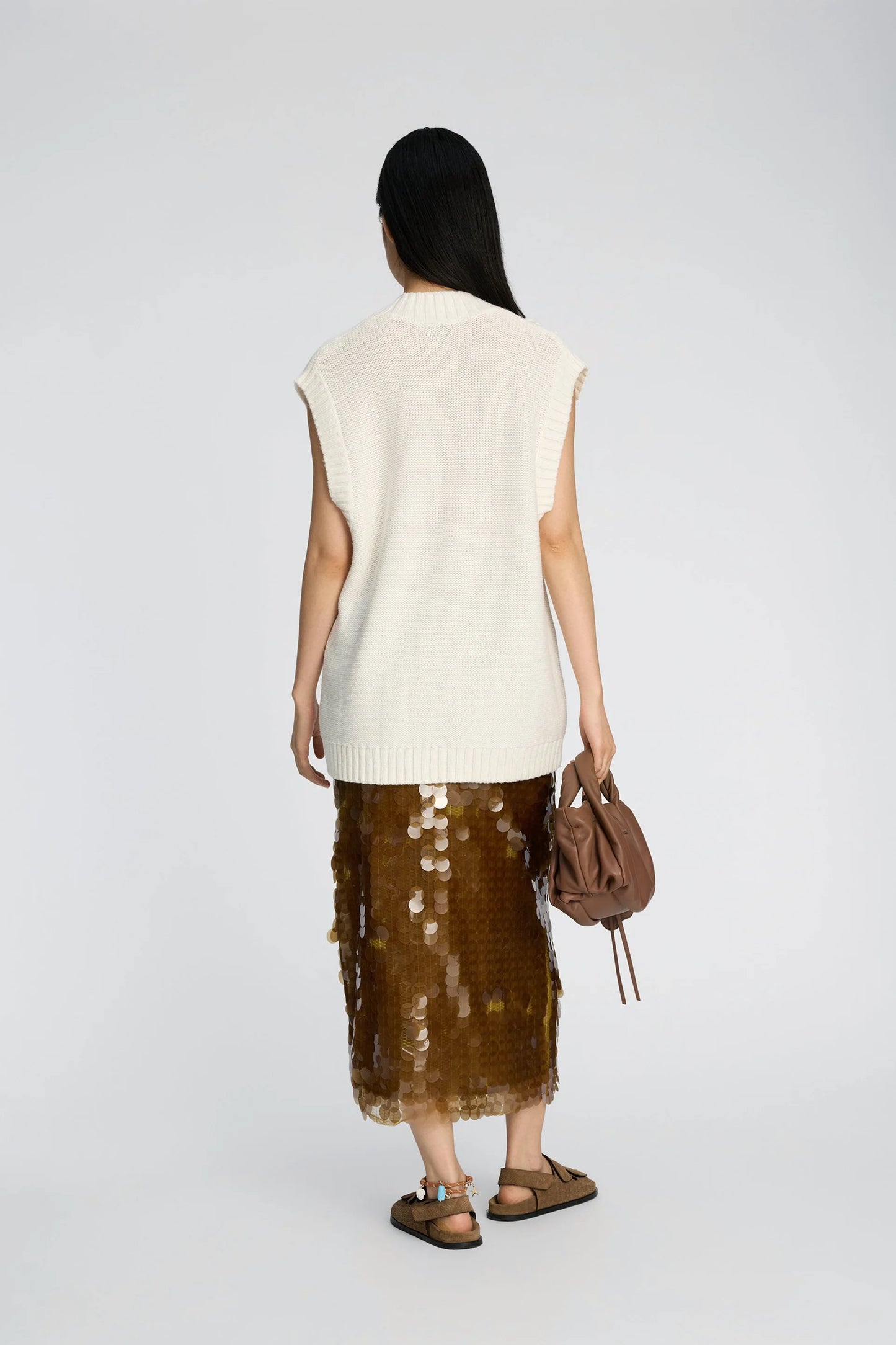 Person wearing a white sleeveless top and brown sequin skirt with a brown handbag on a white background