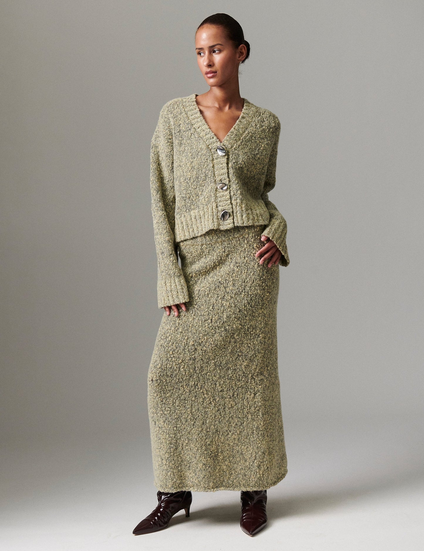 Model facing forward wearing DAY Birger ét Mikkelsen Conor Winter Melange Cardigan in capers green, styled with matching skirt and heeled boots.