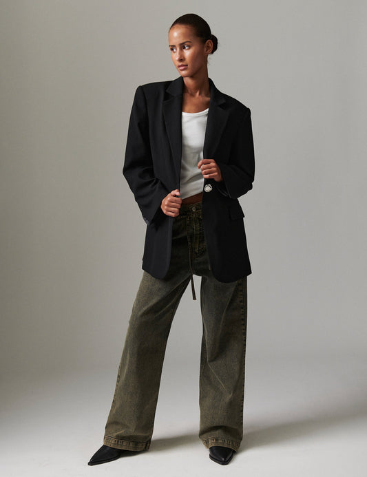 Model wearing DAY Birger ét Mikkelsen Elijah Elm Overdye Denim in elmwood with a white tank top, black oversized blazer, and black pointed-toe shoes.