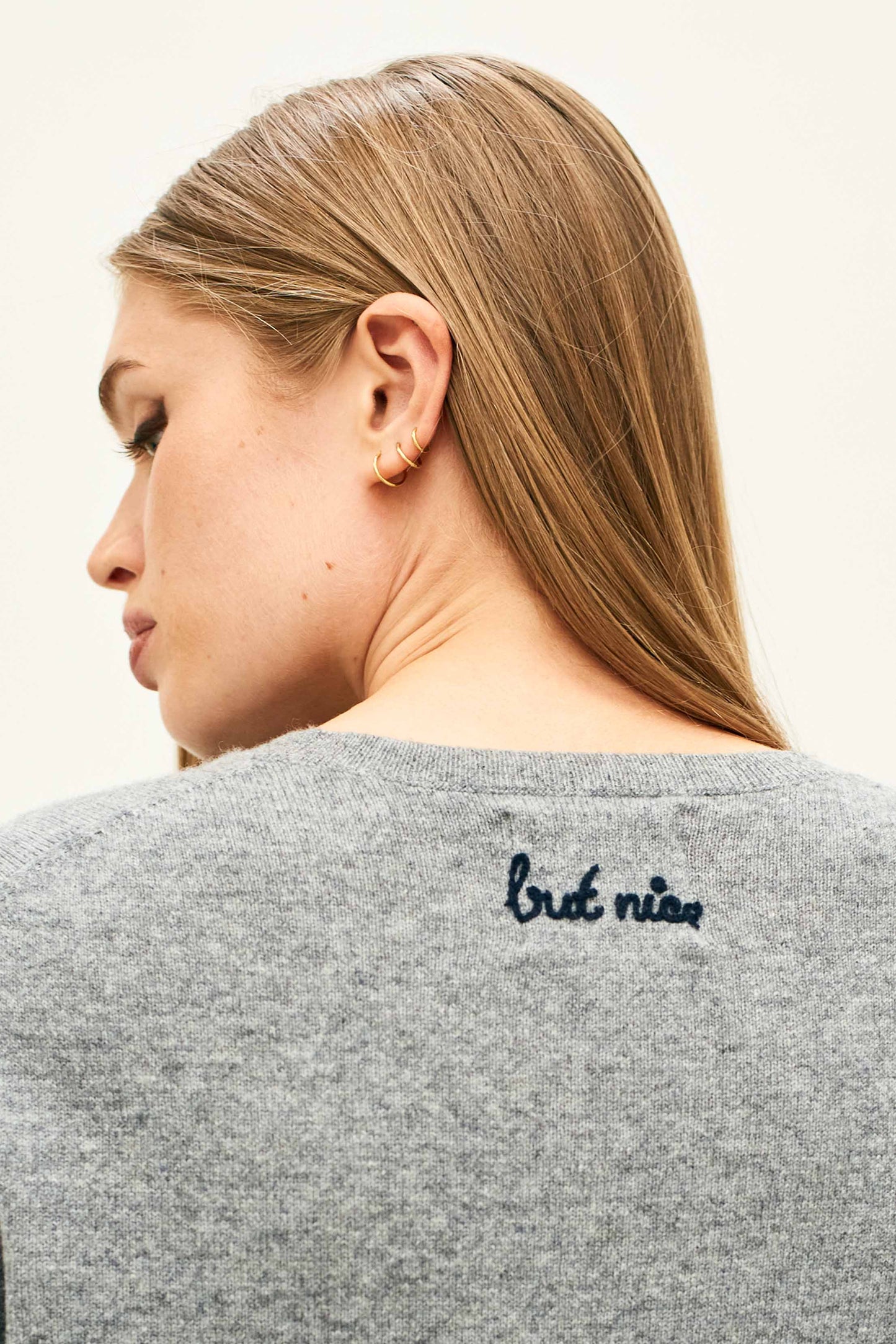 Person wearing a grey sweater with 'but nice' text on the back, against a plain background
