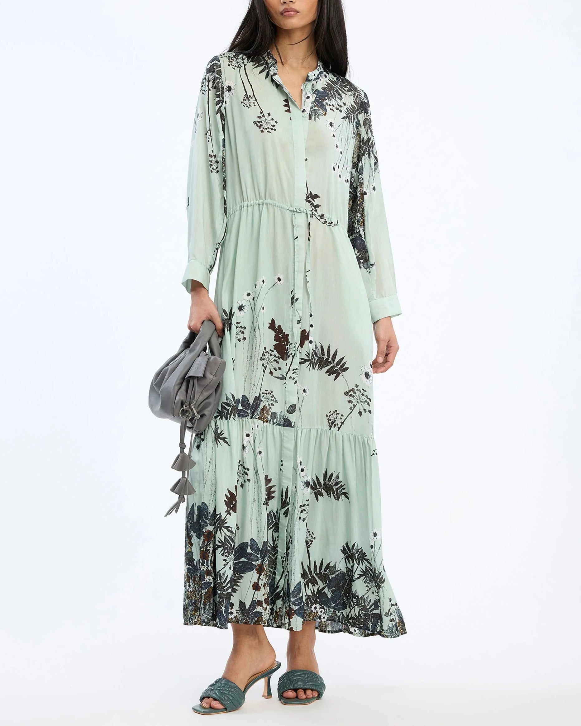Woman wearing a floral dress holding a gray bag on a white background