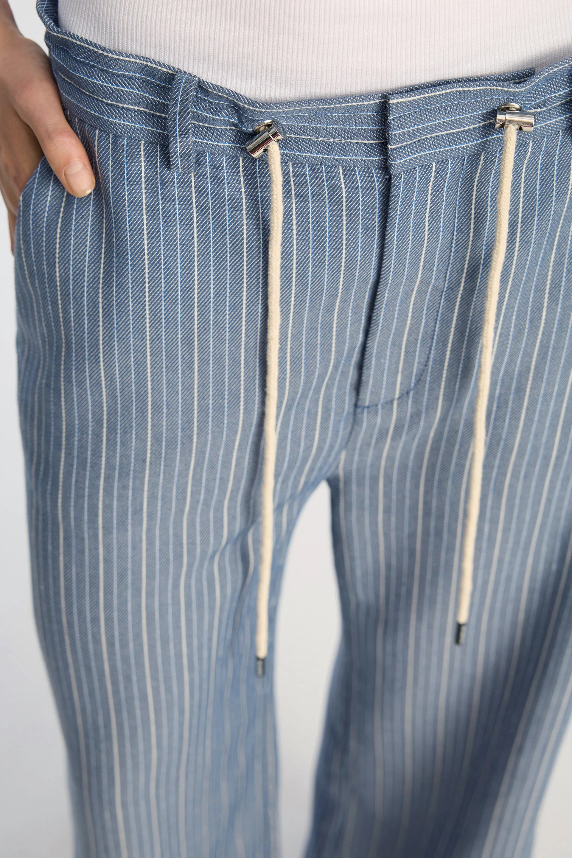 Blue pinstripe pants with drawstring details on a light gray background