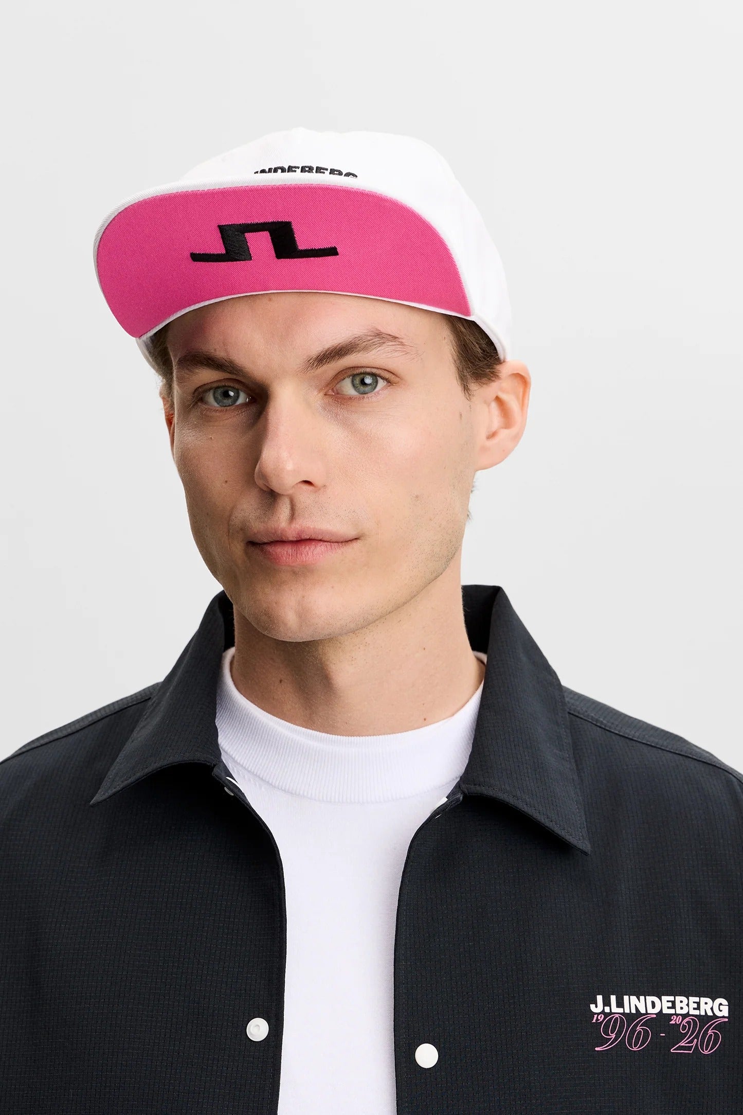 Person wearing a pink and white cap with a logo, black jacket, and white shirt on a white background