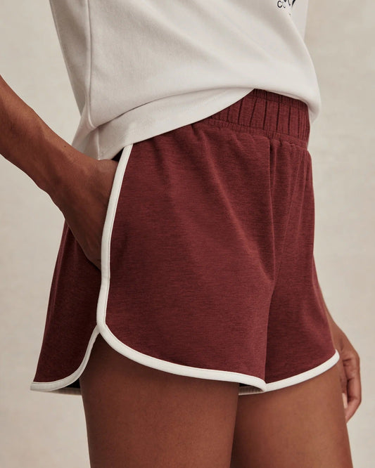 Maroon shorts with white trim worn by a person on a beige background