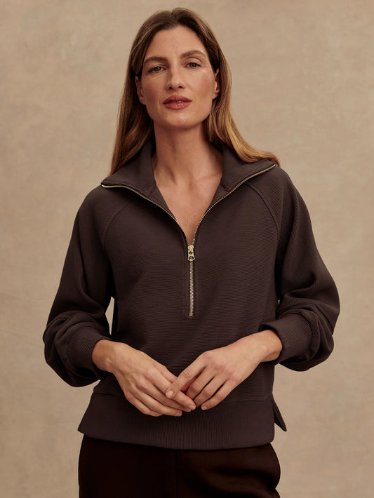 Woman wearing a dark brown zip-up sweatshirt against a beige background