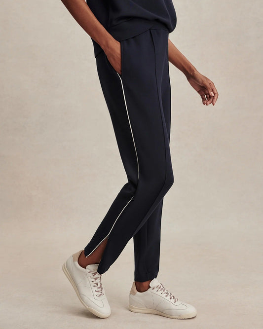 Person wearing navy jogger pants with white stripes on a beige background