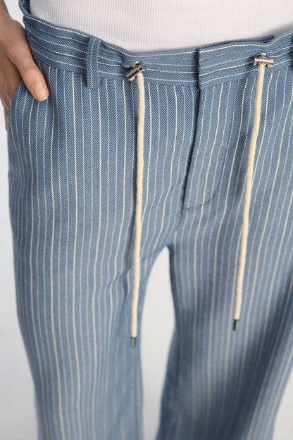 Blue pinstripe pants with drawstring details on a light gray background