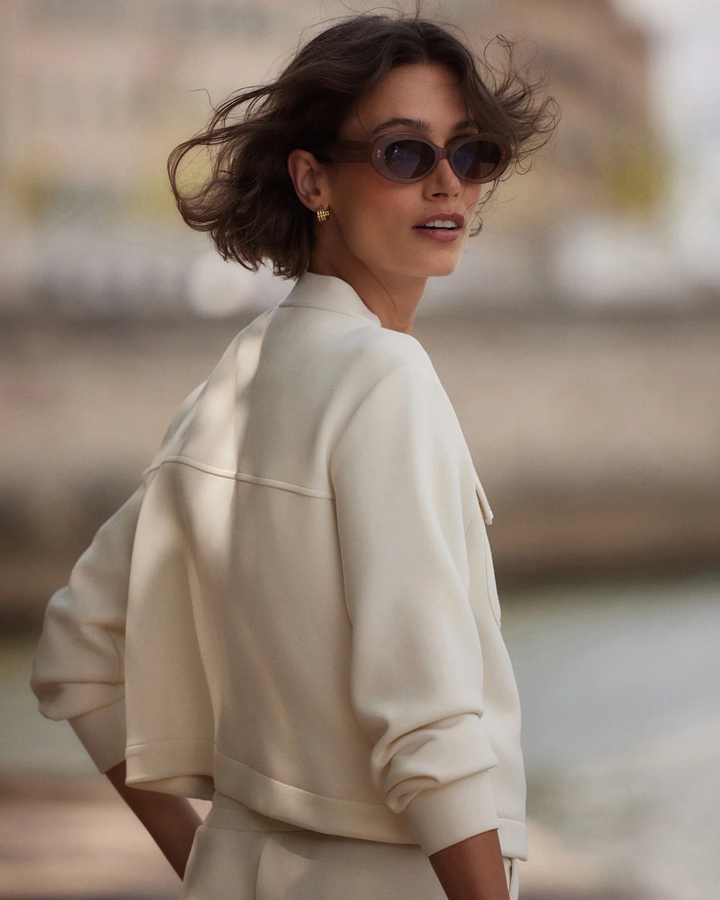 Woman wearing a beige jacket and sunglasses with a blurred background